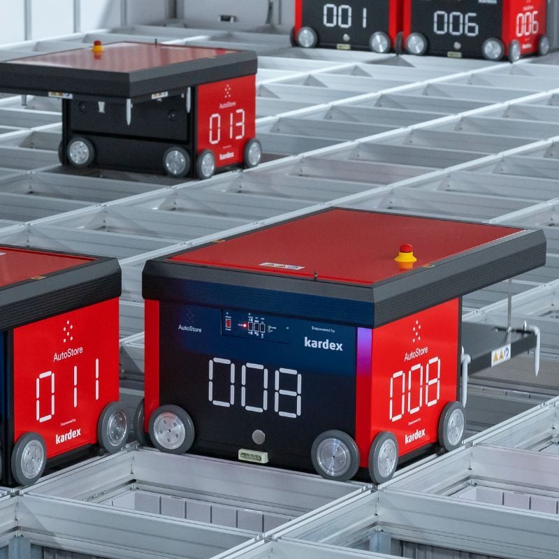 Red and black AutoStore robots on top of aluminum inventory grid